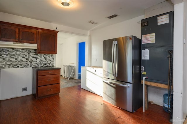 kitchen with dark wood-style flooring, visible vents, backsplash, freestanding refrigerator, and under cabinet range hood