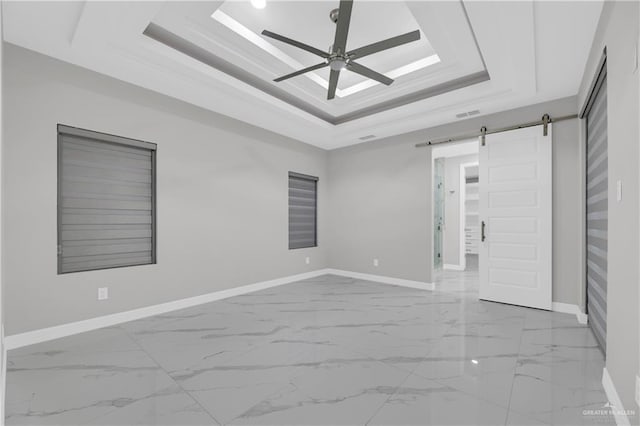 unfurnished room with ceiling fan, a tray ceiling, and a barn door