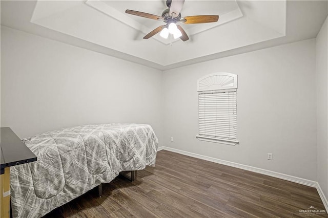 bedroom featuring a raised ceiling, baseboards, and wood finished floors