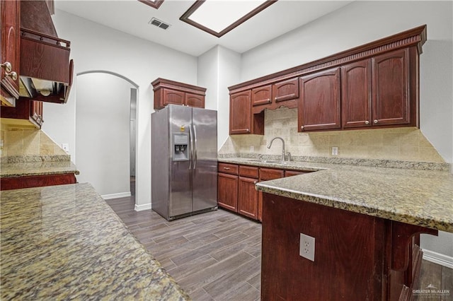 kitchen with stainless steel fridge, arched walkways, dark wood-type flooring, a sink, and backsplash