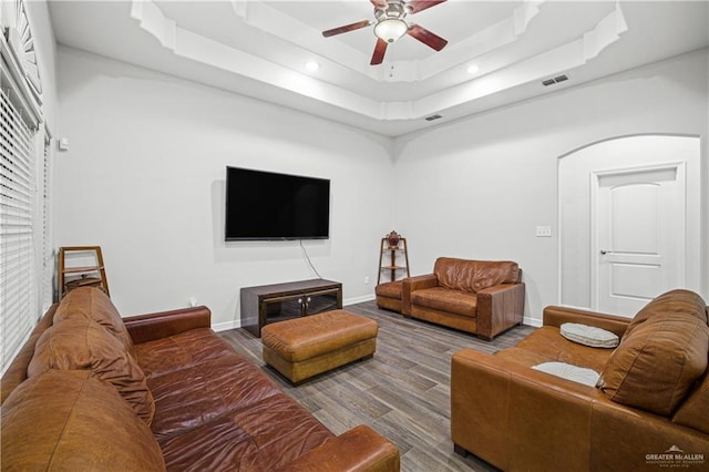 living area featuring a raised ceiling, visible vents, ceiling fan, wood finished floors, and baseboards