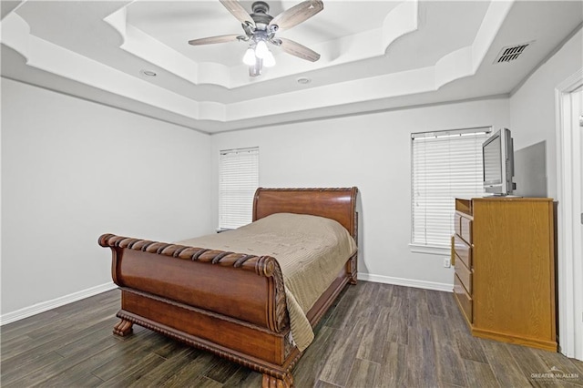 bedroom with dark wood finished floors, a raised ceiling, visible vents, and baseboards