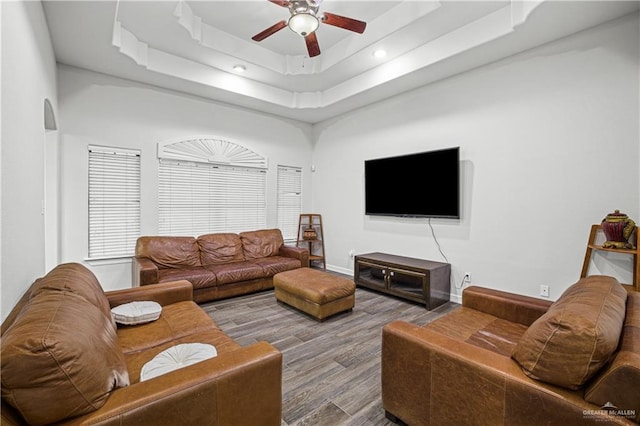 living area featuring arched walkways, ceiling fan, wood finished floors, baseboards, and a tray ceiling