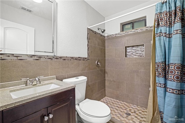 full bathroom featuring toilet, vanity, visible vents, tile walls, and tiled shower