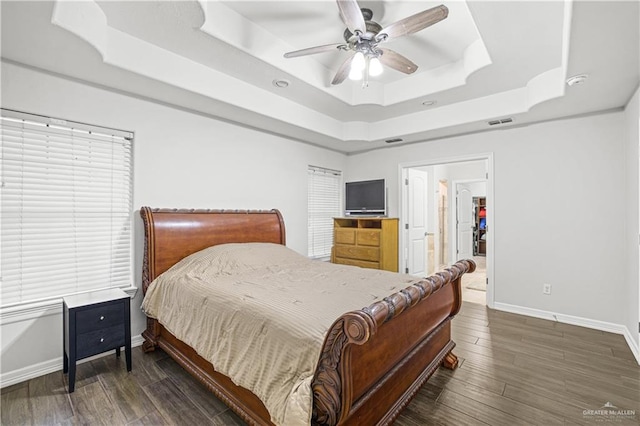 bedroom with baseboards, visible vents, a ceiling fan, wood finished floors, and a tray ceiling