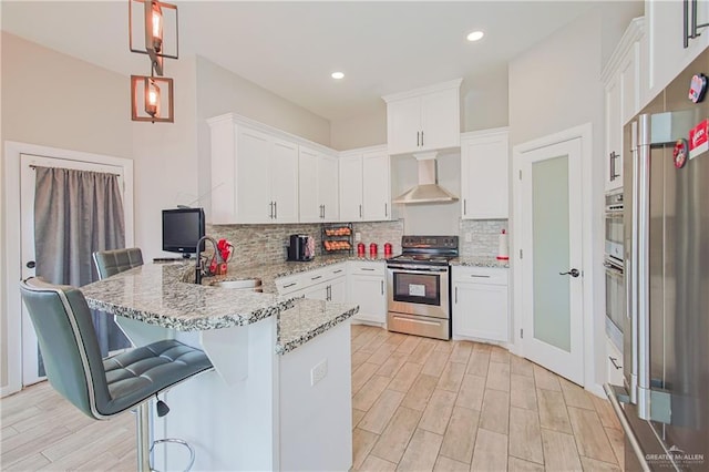 kitchen with wall chimney exhaust hood, appliances with stainless steel finishes, a peninsula, white cabinetry, and a sink