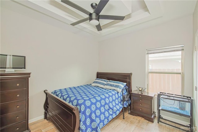 bedroom featuring a ceiling fan, a tray ceiling, light wood-style flooring, and baseboards