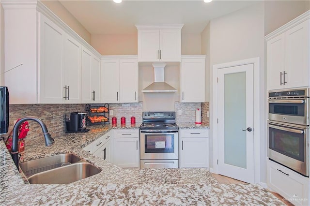 kitchen featuring white cabinets, wall chimney exhaust hood, stainless steel appliances, and a sink