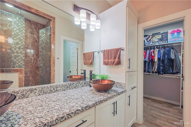 bathroom featuring baseboards, wood finished floors, a walk in closet, vanity, and a shower stall