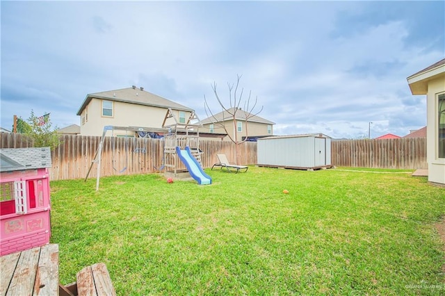 view of yard with a storage shed, a fenced backyard, a playground, and an outbuilding