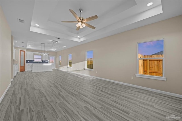 spare room with ceiling fan, a tray ceiling, and light wood-type flooring