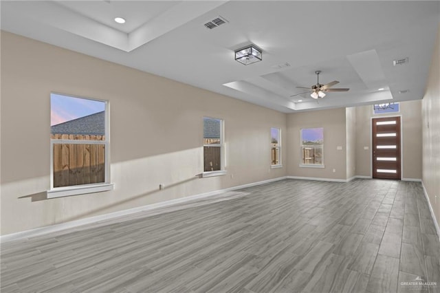 unfurnished living room with ceiling fan, a raised ceiling, and light wood-type flooring