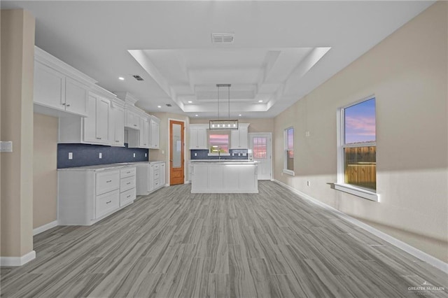 kitchen with tasteful backsplash, a raised ceiling, hanging light fixtures, white cabinets, and sink