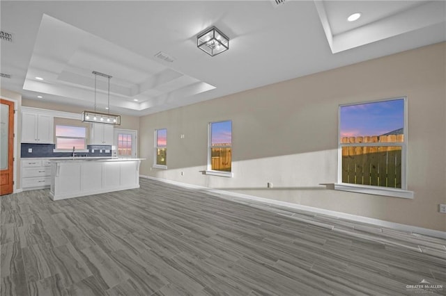 kitchen featuring a center island, a raised ceiling, pendant lighting, sink, and white cabinetry