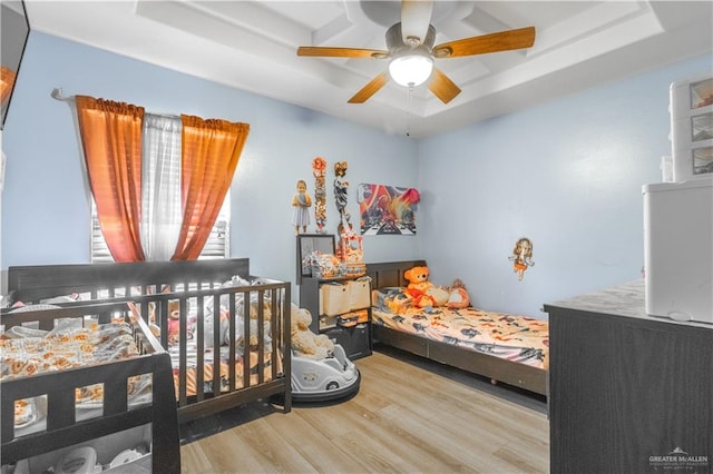 bedroom with a tray ceiling, ceiling fan, and light wood-type flooring