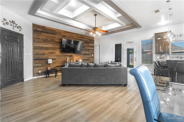 living room featuring a raised ceiling, wood walls, ceiling fan, and light hardwood / wood-style floors