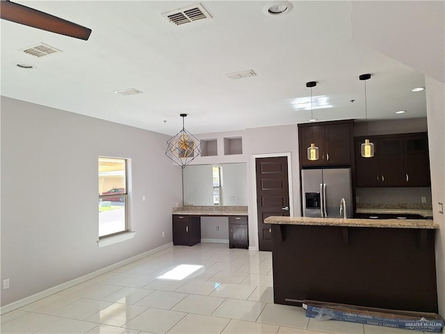 kitchen with dark brown cabinetry, backsplash, stainless steel fridge, decorative light fixtures, and light tile patterned floors