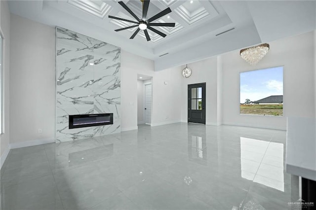 unfurnished living room featuring ceiling fan with notable chandelier, a high end fireplace, and coffered ceiling