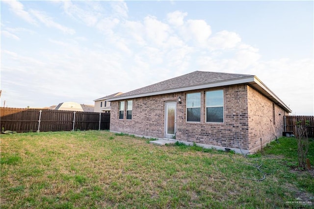 rear view of property with a yard, brick siding, roof with shingles, and a fenced backyard