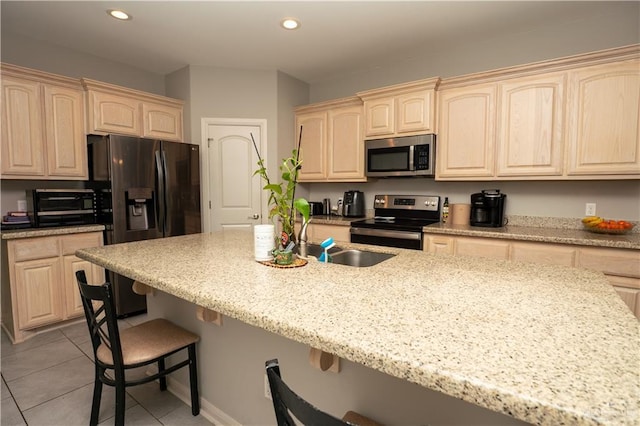 kitchen with a breakfast bar area, recessed lighting, light brown cabinetry, appliances with stainless steel finishes, and light tile patterned flooring