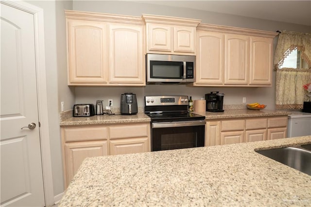 kitchen with a sink, appliances with stainless steel finishes, light brown cabinets, and light stone counters