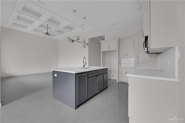 kitchen with coffered ceiling, a kitchen island with sink, beam ceiling, white cabinets, and sink