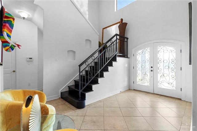 entryway featuring french doors, a towering ceiling, a healthy amount of sunlight, and light tile patterned floors