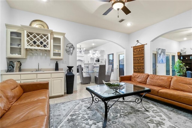 living room with light tile patterned flooring, ceiling fan with notable chandelier, and wet bar