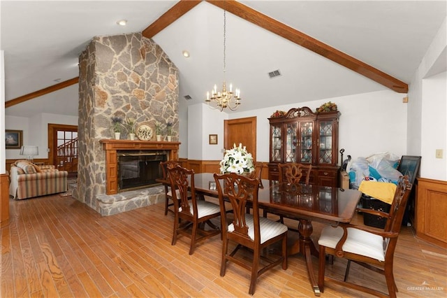 dining area with lofted ceiling with beams, light hardwood / wood-style floors, a stone fireplace, and a notable chandelier