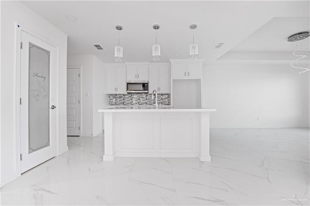 kitchen featuring white cabinetry, backsplash, a center island with sink, and pendant lighting