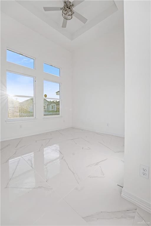 empty room with ceiling fan and a raised ceiling