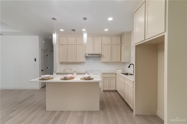 kitchen featuring decorative light fixtures, sink, a center island, cream cabinets, and light hardwood / wood-style flooring