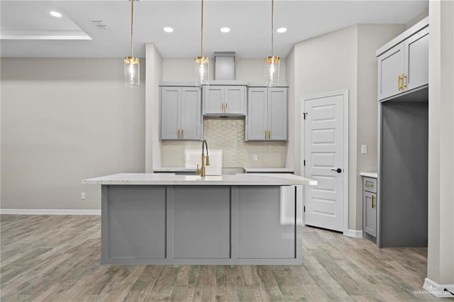 kitchen with pendant lighting, an island with sink, and gray cabinetry