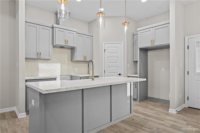 kitchen featuring light hardwood / wood-style flooring, a kitchen island with sink, backsplash, gray cabinetry, and decorative light fixtures