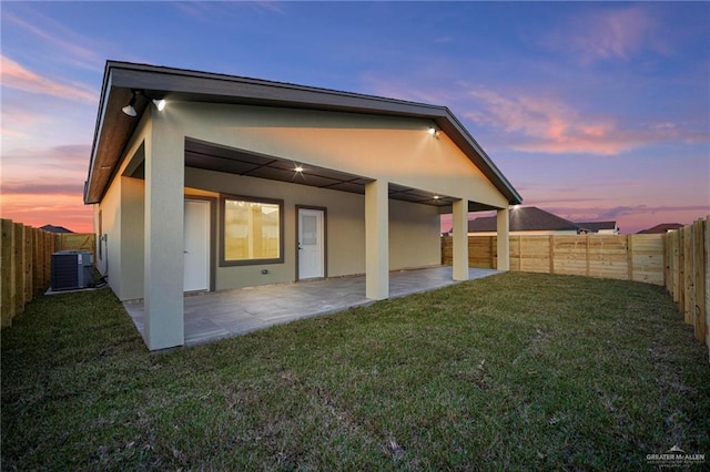 back house at dusk with cooling unit, a patio area, and a lawn