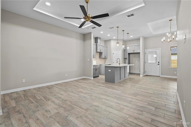 unfurnished living room featuring a raised ceiling, sink, ceiling fan with notable chandelier, and light hardwood / wood-style floors