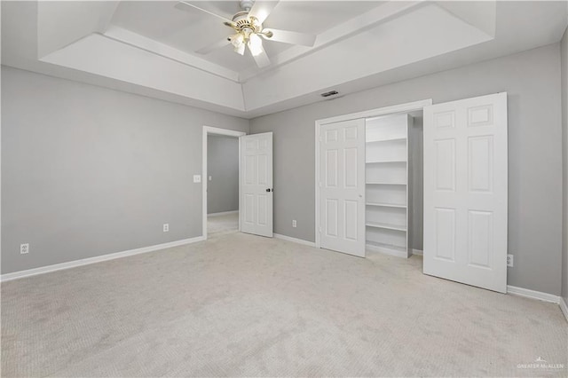 unfurnished bedroom featuring ceiling fan, light colored carpet, a tray ceiling, and a closet