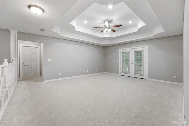 carpeted spare room with a raised ceiling, ceiling fan, and french doors