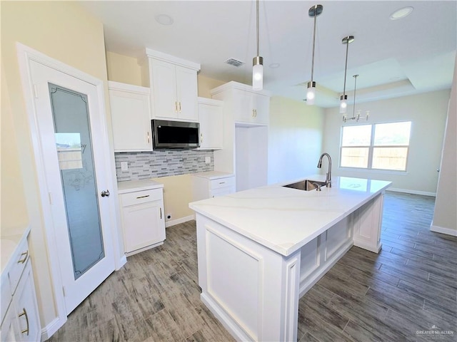 kitchen with sink, pendant lighting, a kitchen island with sink, decorative backsplash, and white cabinets