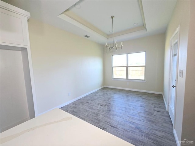 unfurnished dining area with dark hardwood / wood-style floors, a chandelier, and a tray ceiling