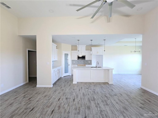 kitchen featuring white cabinetry, an island with sink, sink, hanging light fixtures, and light hardwood / wood-style floors