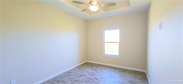 spare room featuring ceiling fan, light wood-type flooring, and a tray ceiling