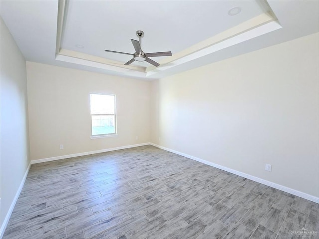 empty room featuring a raised ceiling, ceiling fan, and light hardwood / wood-style flooring