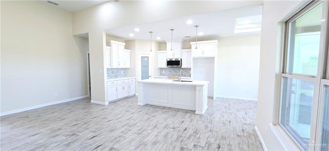 kitchen with decorative light fixtures, tasteful backsplash, white cabinetry, a center island with sink, and light hardwood / wood-style flooring