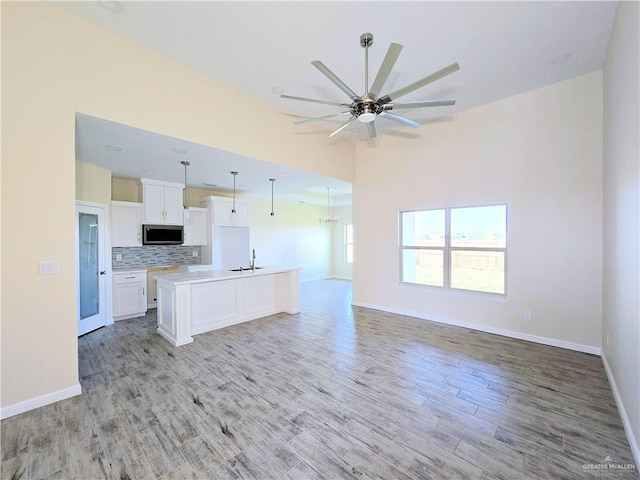 kitchen with pendant lighting, sink, white cabinetry, tasteful backsplash, and an island with sink