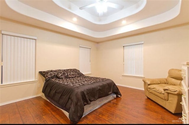 bedroom with ceiling fan, dark hardwood / wood-style floors, and a tray ceiling