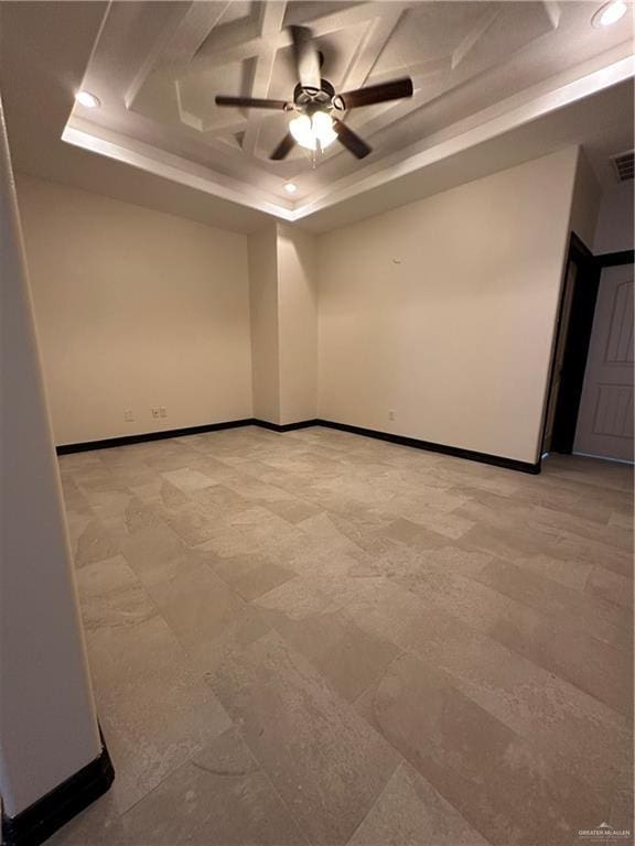 empty room with ceiling fan and a tray ceiling