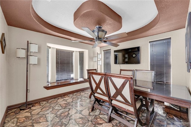 613 E Moore Rd, San Juan, TX 78589 - dining room featuring stone finish flooring, baseboards, ceiling fan, and a tray ceiling