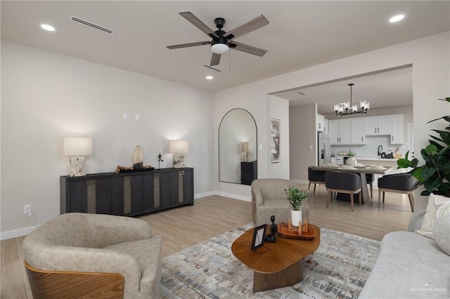 living room featuring sink, ceiling fan with notable chandelier, and light hardwood / wood-style flooring