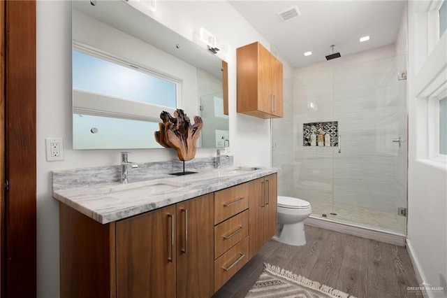 bathroom featuring visible vents, double vanity, wood finished floors, toilet, and a stall shower